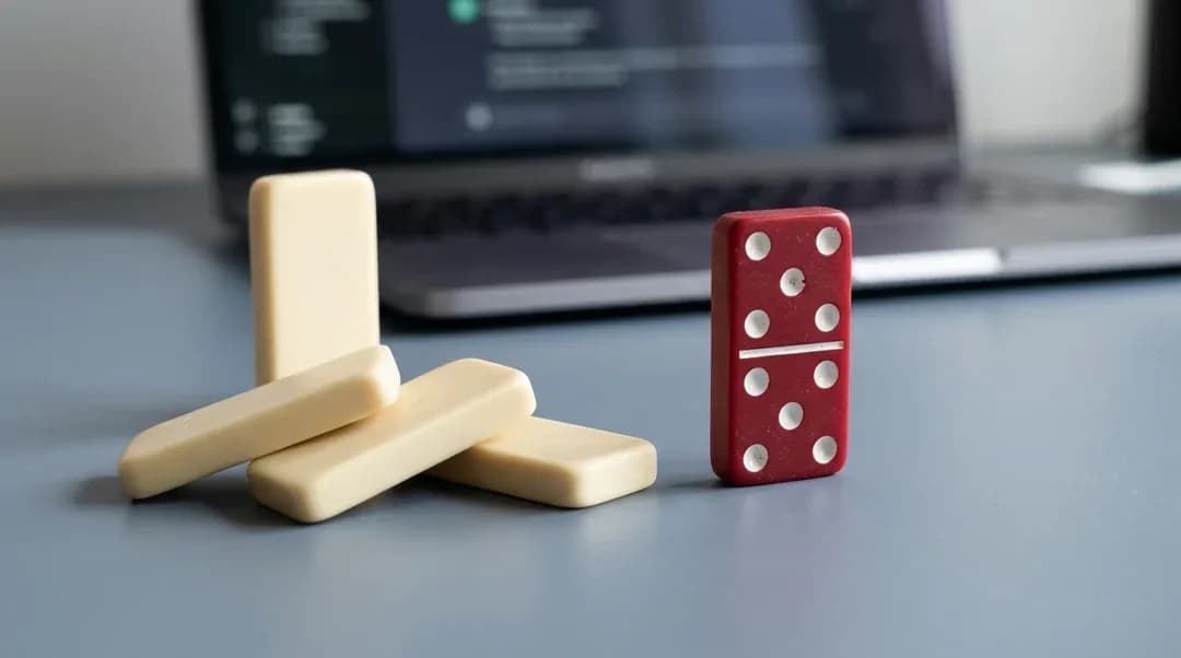 Dominoes falling towards a red die in front of a laptop