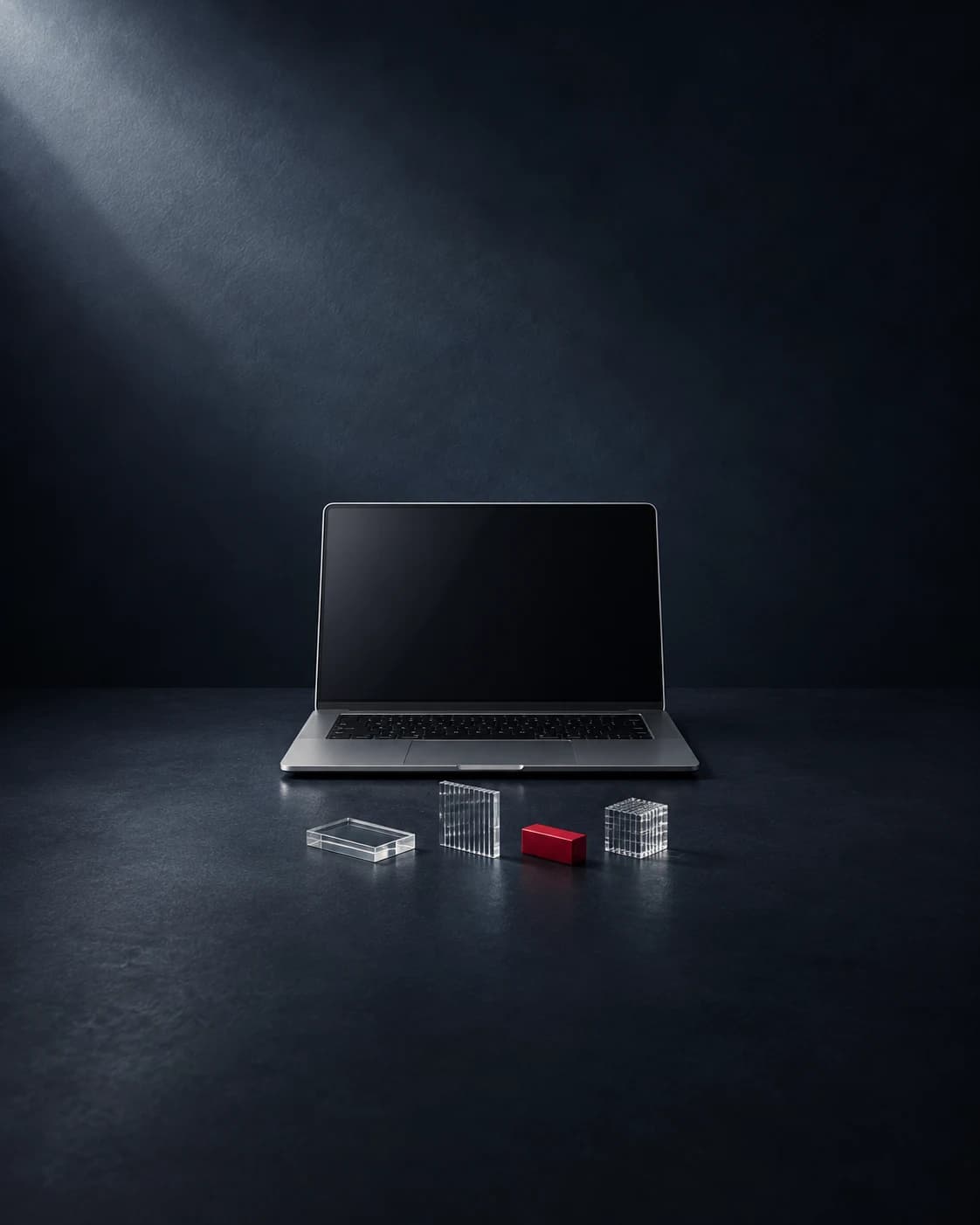 Conceptual AgentShield artwork showing a complete laptop set back on a charcoal surface, with clear glass pieces and a carmine red block.